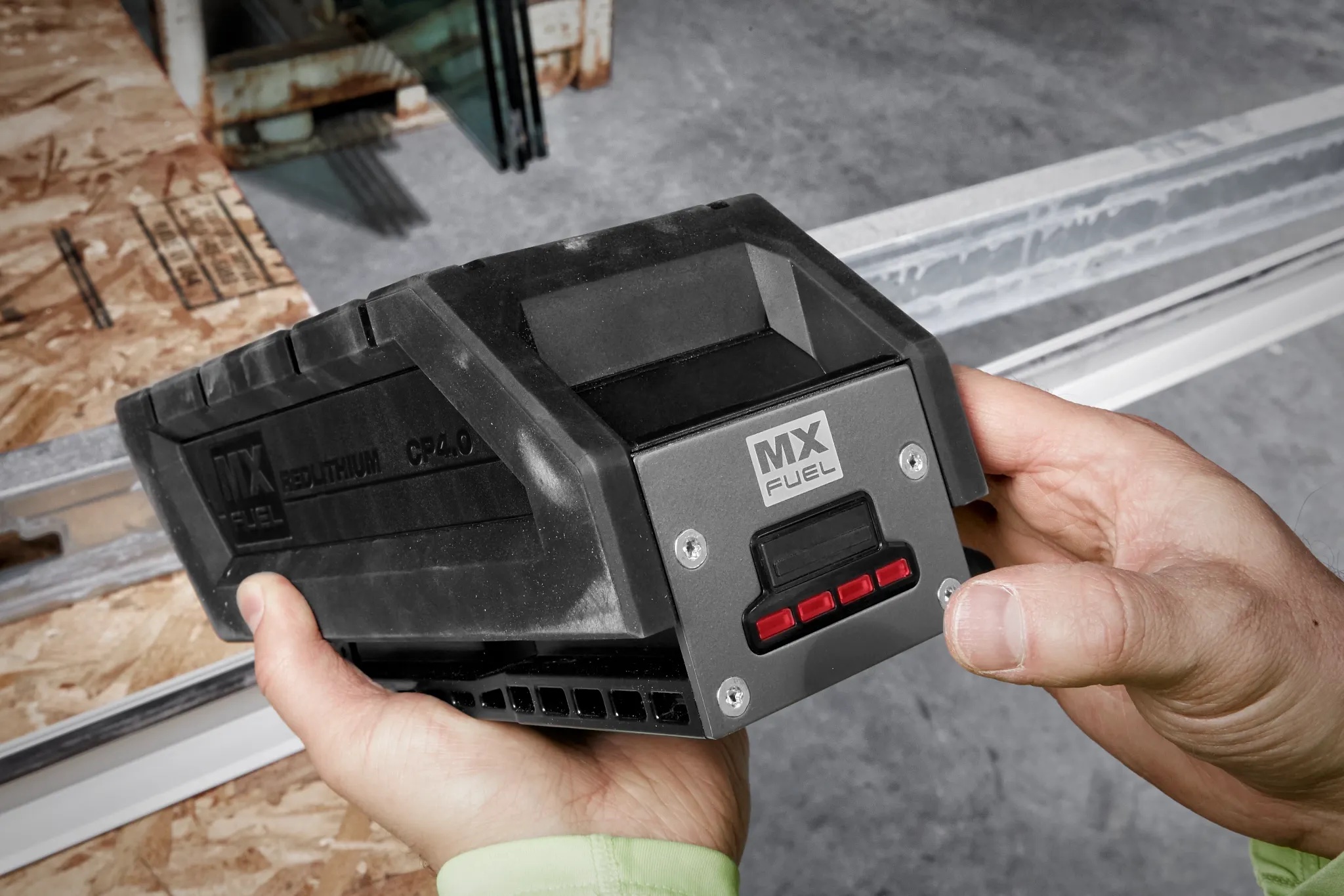 Two hands holding a Milwaukee MX FUEL REDLITHIUM CP4.0 battery pack with its red fuel gauge lit, on a jobsite