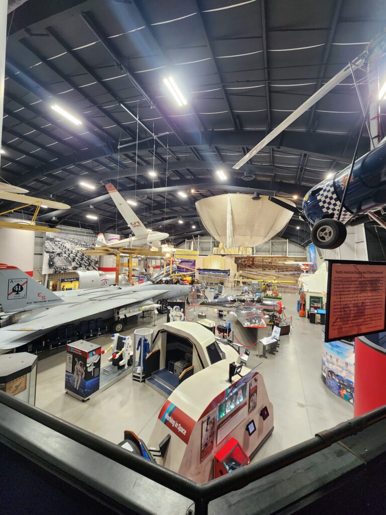 View across the Tulsa Air & Space Museum exhibit hall showing a jet, hanging aircraft, a flight simulator and display panels under high-bay lighting