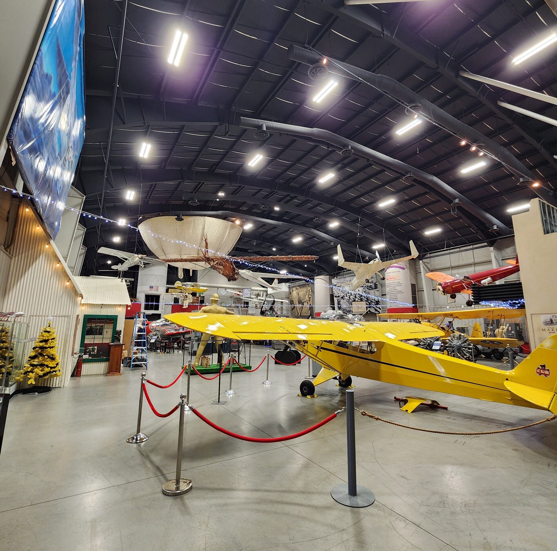 A yellow vintage aircraft behind a red rope barrier inside the Tulsa Air & Space Museum hangar, with LED fixtures lighting the high ceiling