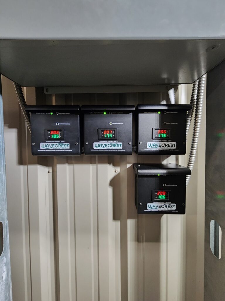 Four black Wavecrest power quality protection units with digital voltage and amperage displays mounted on a panel wall, wired with flexible conduit, at the Tulsa Air & Space Museum