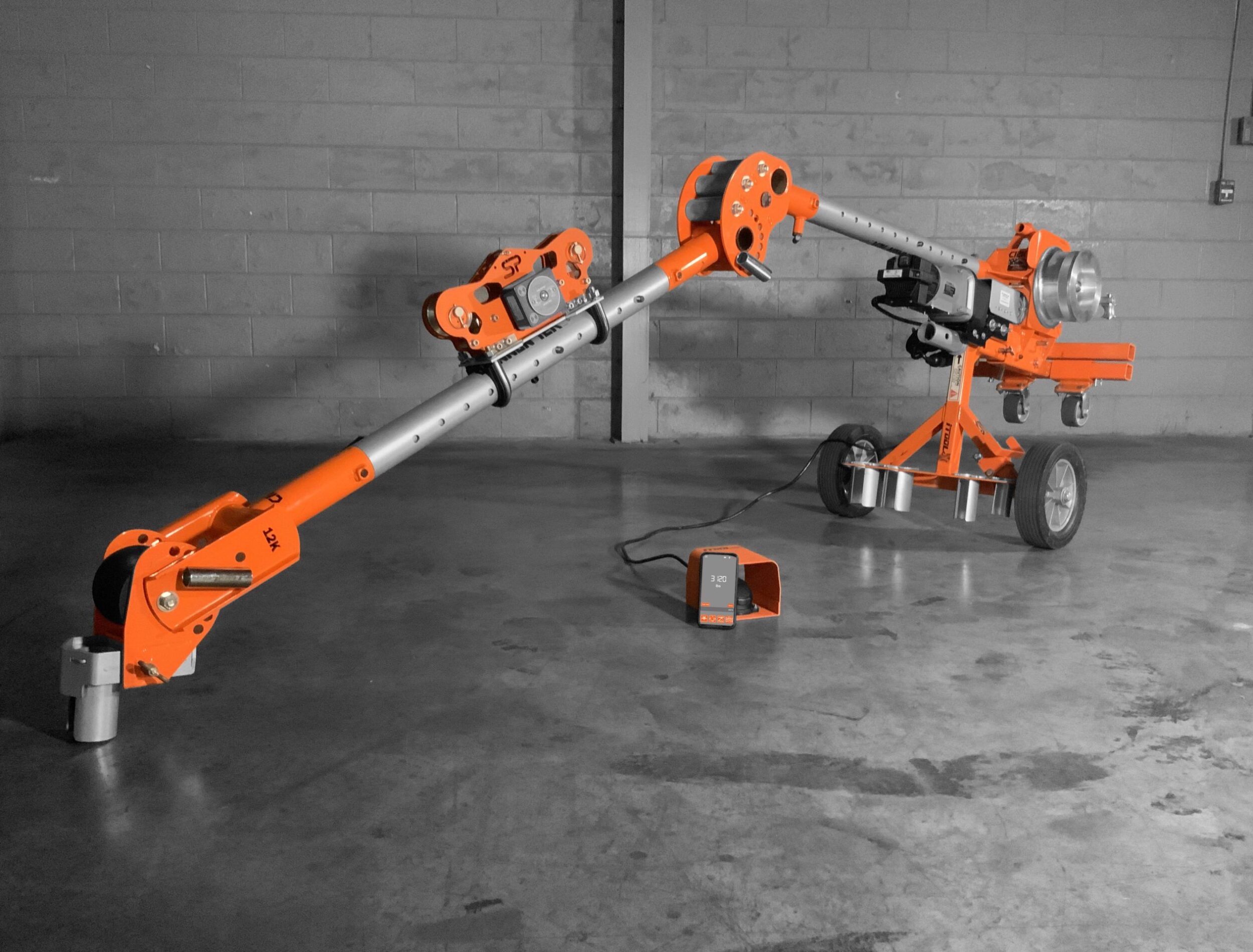 iTOOLco Safe Pull RLT SPRLT20K orange running line tension meter set up with cable-pulling equipment on a concrete jobsite floor, with its carrying case nearby