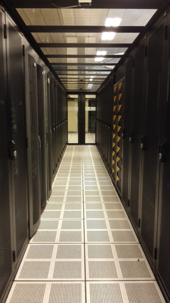 Long aisle between rows of black server cabinets over a perforated raised floor in a brightly lit data center